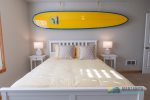 The queen bed with a decorative surfboard, side tables, and lamps.